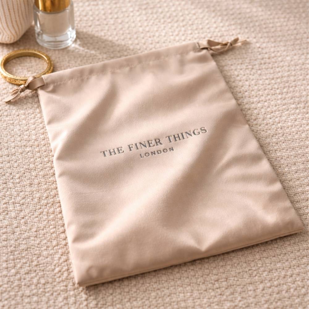 Beige drawstring bag with 'The Finer Things London' branding on a beige surface.
