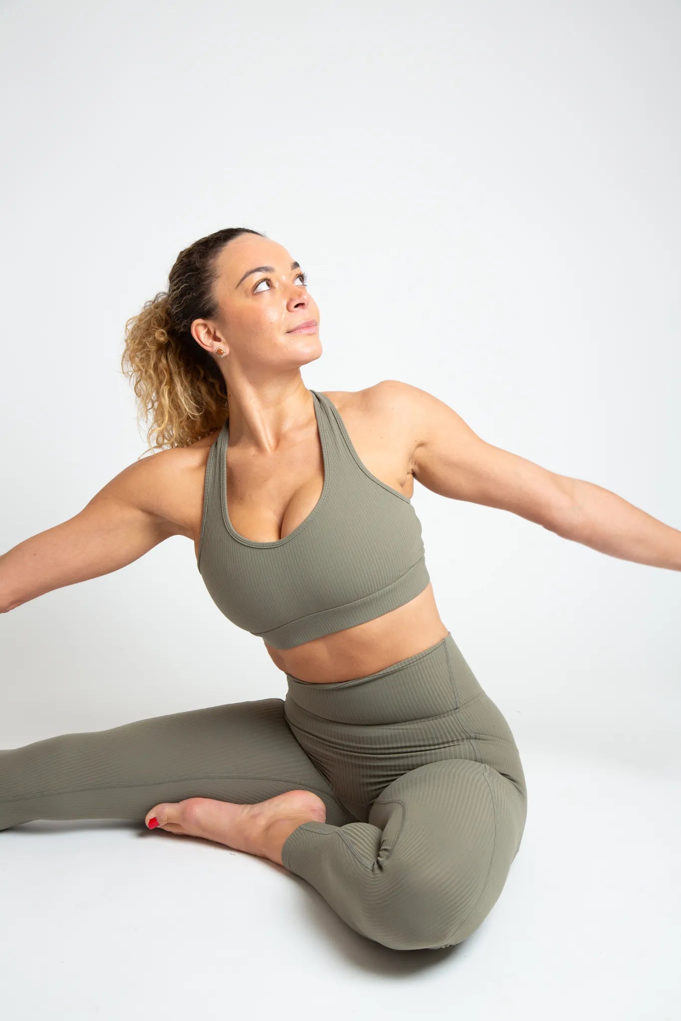 Woman in olive green sports bra and leggings sitting on a white background
